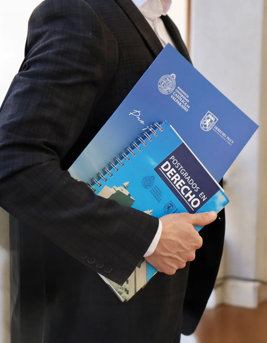 Persona sosteniendo material académico de los postgrados en Derecho PUCV